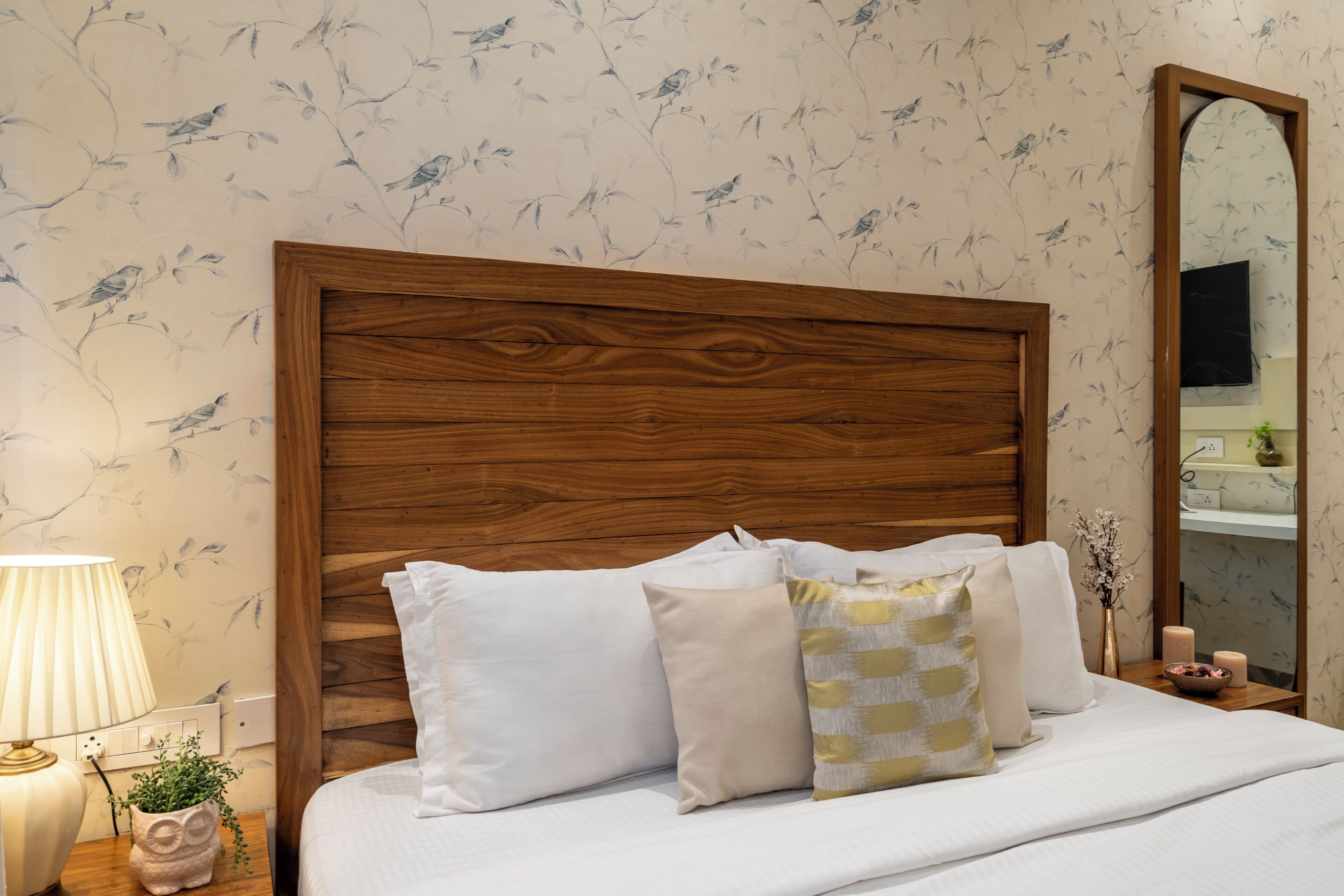 Un dormitorio con cabecera de madera, ropa de cama blanca y un espejo en la pared.