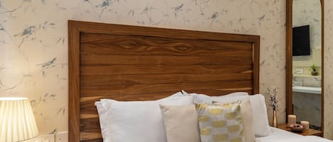 A bedroom with a wooden headboard, white bedding, and a mirror on the wall.