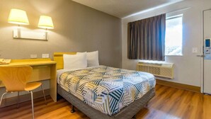 Una habitació d'hotel amb un llit, escriptori, cadira, finestra amb cortines i una porta.