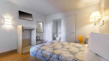 A hotel room with a bed, a desk, a chair, a toilet, and a mirror.