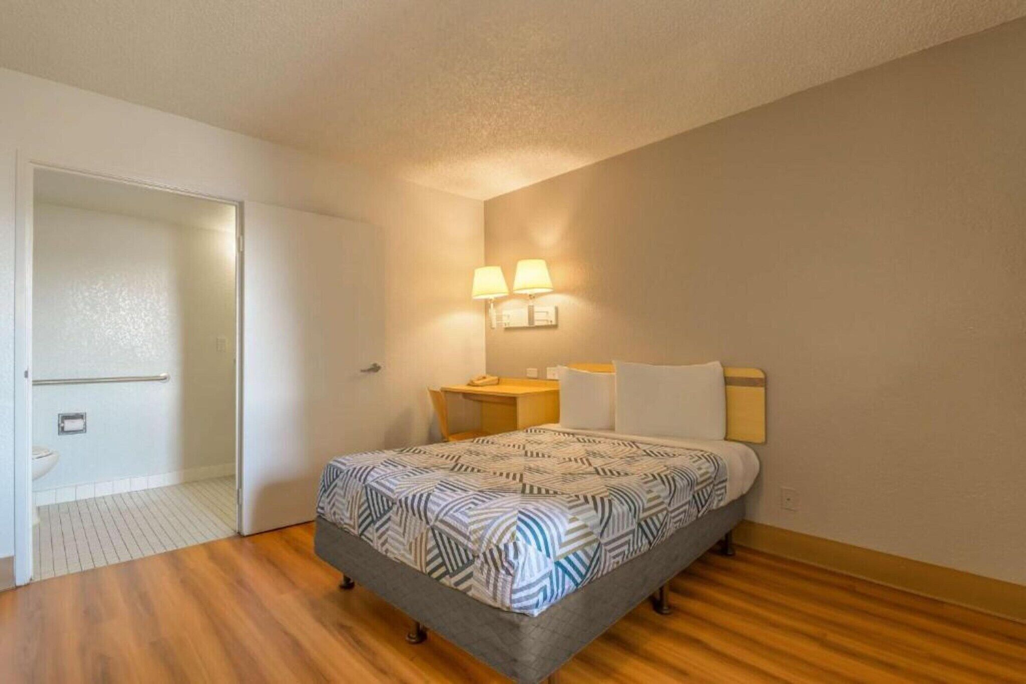 A bedroom with a bed, bedside lamps, a small table, and a door leading to a bathroom.