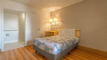 A bedroom with a bed, bedside lamps, a small table, and a door leading to a bathroom.