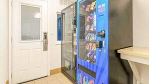 Ein Getränkeautomat mit Snacks, eine weiße Tür und ein kleiner Tisch.