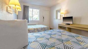 A hotel room with two beds, a television, and a window with curtains.