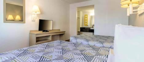 A hotel room with two beds, a television on a stand, and a mirror on the wall.
