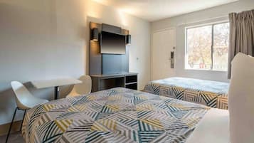 Hotellihuone, jossa on kaksi sänkyä, työpöytä, tuoli, televisio ja ikkuna.