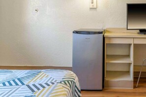 Une chambre comprenant un lit, un petit réfrigérateur, un bureau avec un ordinateur et une étagère.