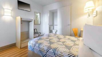 A hotel room with a bed, a chair, a TV, a mirror, and a door leading to a bathroom.