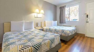 Hotellihuone, jossa on kaksi sänkyä, ikkuna verhoilla, yöpöytä ja seinään kiinnitetyt lamput.