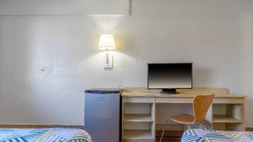 A hotel room with a bed, a desk with a computer, a chair, and a trash bin.