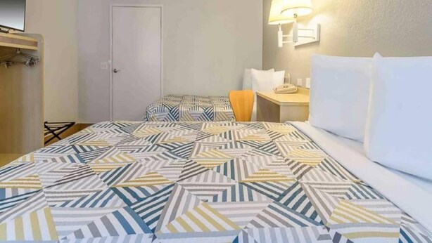 Une chambre d’hôtel avec un lit, un bureau, une chaise et une armoire.