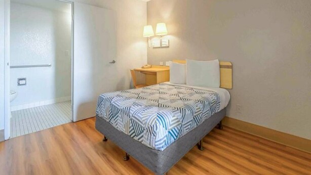 Un dormitorio con cama, mesita de noche, lámpara y una puerta que da a otra habitación.