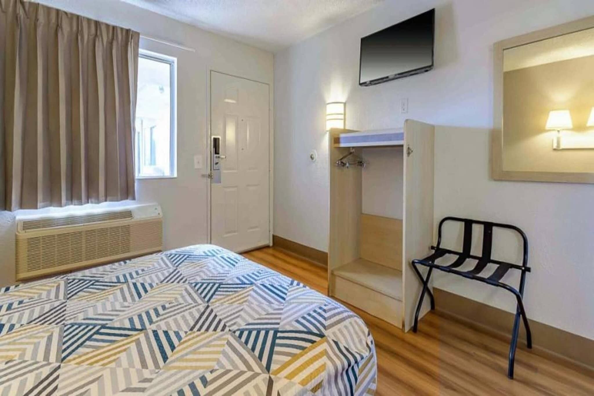 A hotel room with a bed, a chair, a wardrobe, a television, and a window with curtains.
