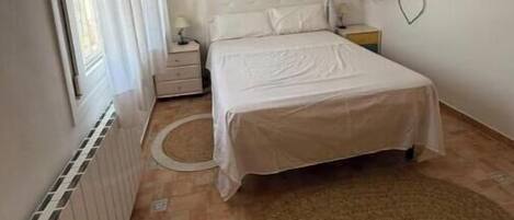 A bedroom with a bed, a nightstand, a lamp, a radiator, and a window with curtains.