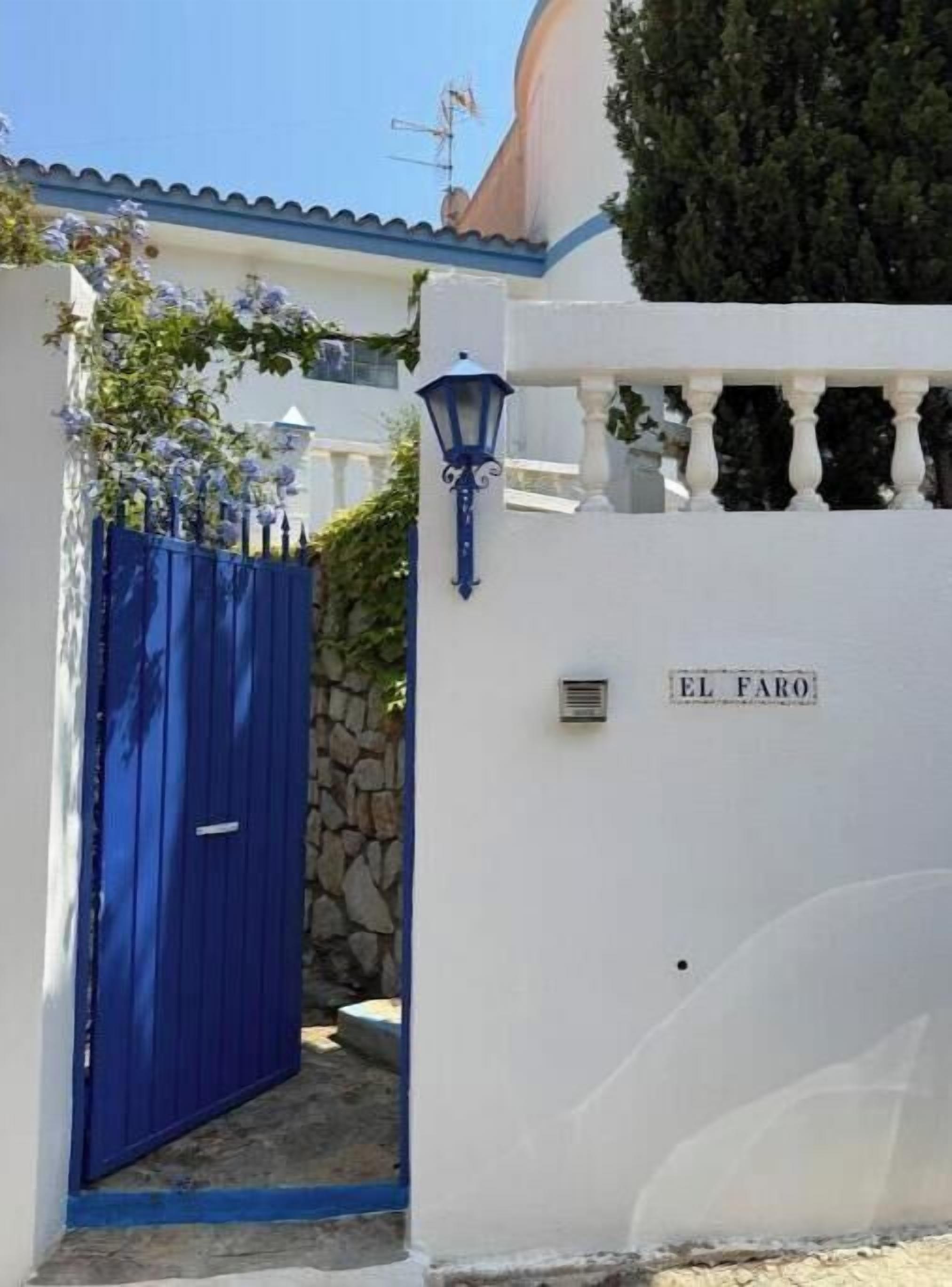 A white building with a blue gate, a stone wall, and a lamp post.