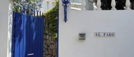 A white building with a blue gate, a stone wall, and a lamp post.