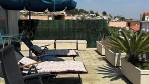 En tagterrasse med liggestole og en stor parasol med udsigt over et boligområde.