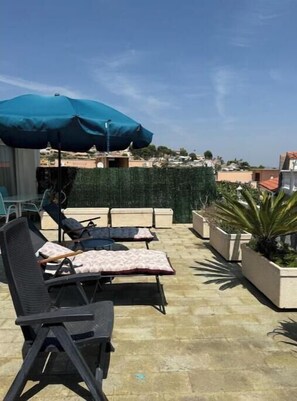Eine Dachterrasse mit Liegestühlen und einem großen Sonnenschirm mit Blick auf ein Wohngebiet.
