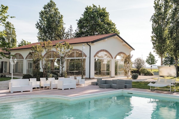 A poolside area with outdoor seating, a swimming pool, and a building with arched windows.