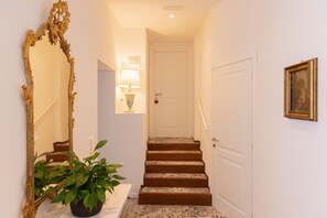 A hallway with a staircase, a mirror, a wall-mounted lamp, a door, and a framed picture.