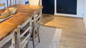 Un comedor con mesa y sillas de madera, una cocina con armarios oscuros y una lámpara colgante.