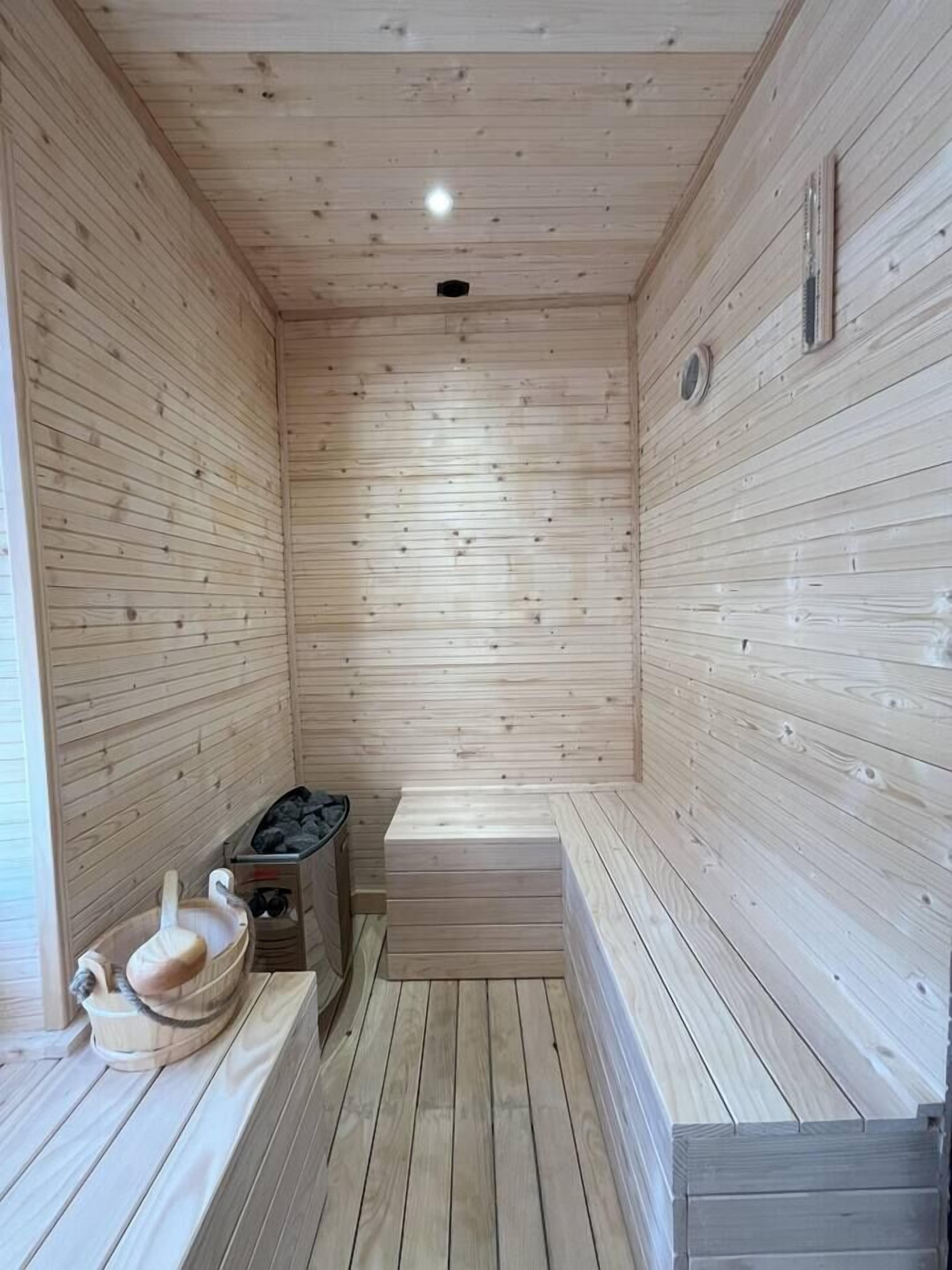 A sauna room with wooden walls and benches, a bench heater, and a small heater on the floor.
