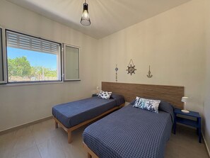 Ein Schlafzimmer mit zwei Betten, einem Fenster mit Jalousien, einer Hängelampe und Wanddekoration im Seestil.