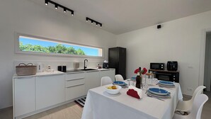 Uma cozinha moderna com área de jantar, armários brancos, uma janela grande e vista para o verde.
