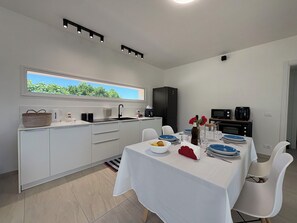 Eine moderne Küche mit Essbereich, weißen Schränken, einem großen Fenster und Blick auf Grünflächen.
