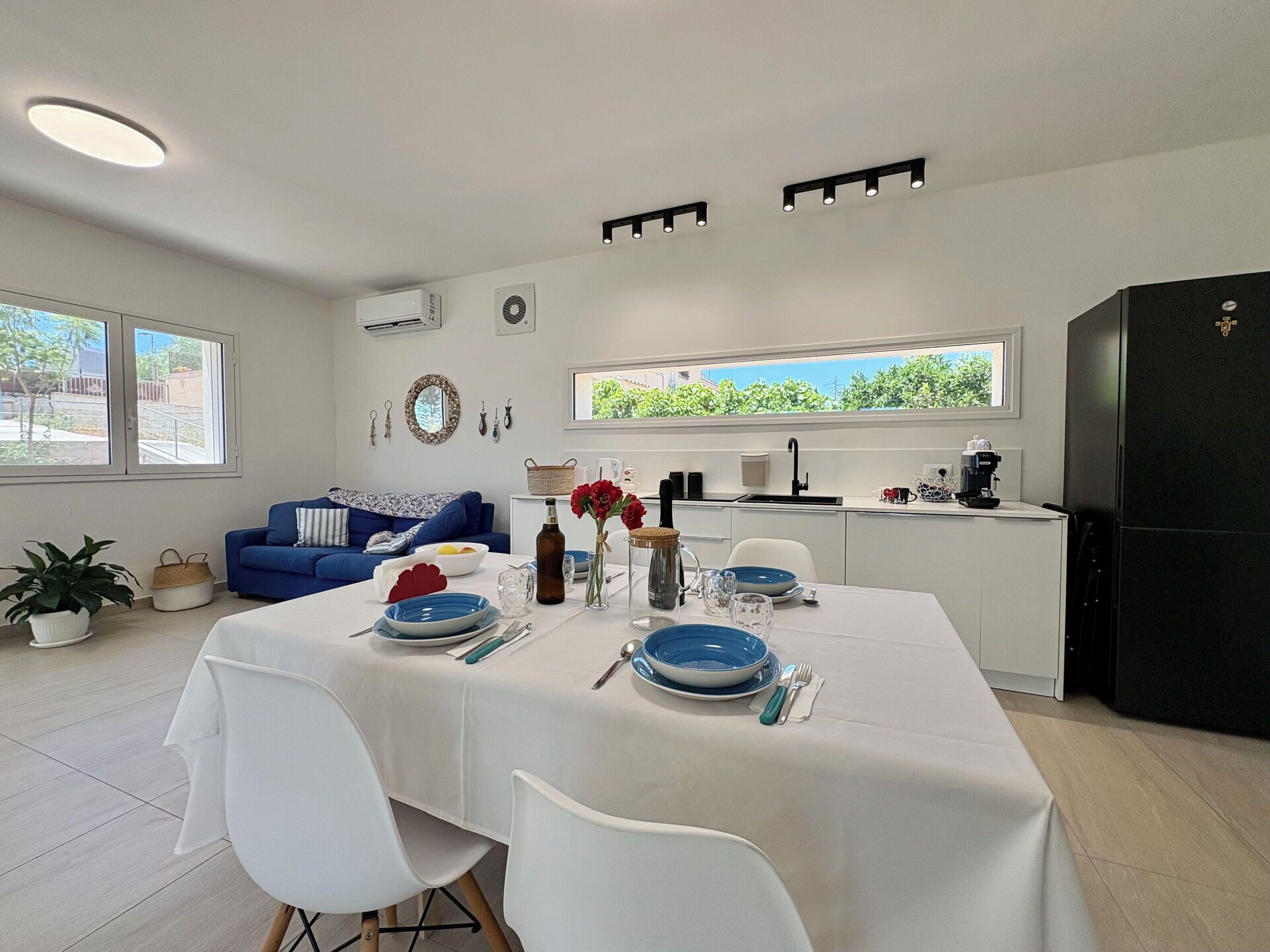 A modern kitchen and dining area with a white table set for two, a blue sofa, and a black refrigerator.