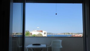En balkong med ett bord och två stolar, med utsikt över ett kustnära område med byggnader och en klar himmel.