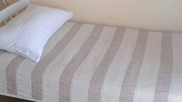 A single bed with a striped bedding pattern, a white pillow, and a plain wall in the background.