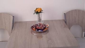 A dining table with four chairs, a vase with a yellow flower, and a bowl of fruit.