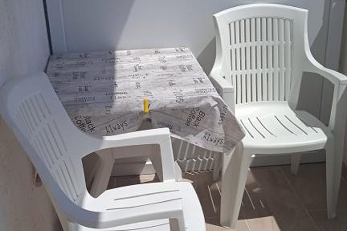 A small outdoor seating area with a table and two white plastic chairs.