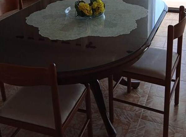 A round dining table with a lace tablecloth, four wooden chairs, and a vase with yellow flowers. - Apartments Balić (Rogoznica)