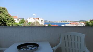 A balcony with a table and chair, overlooking a coastal town with buildings and a clear sky.
