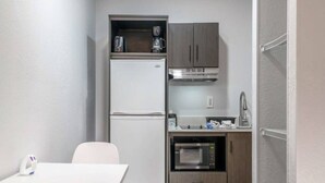 Een compacte kitchenette met een koelkast, magnetron en oven, een klein aanrecht en een stoel.