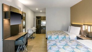 Een hotelkamer met twee bedden, een bureau, een stoel, een kitchenette en een badkamer.