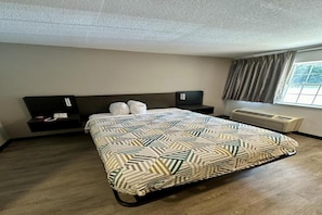 A hotel room with a bed, a nightstand, a heater, and a window with curtains.