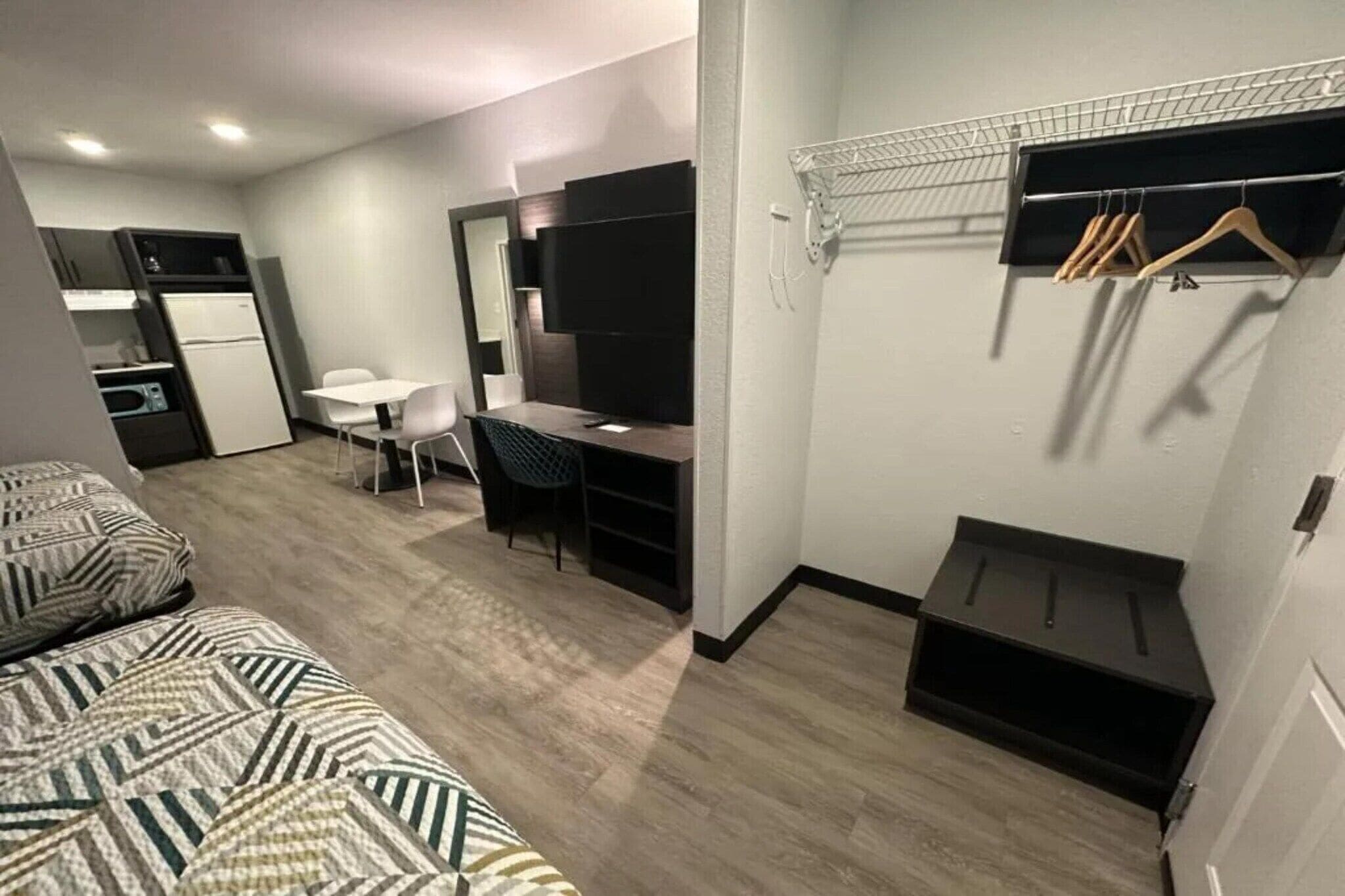 A compact hotel room with a bed, desk, chair, and a small kitchenette.