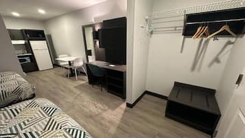A compact hotel room with a bed, desk, chair, and a small kitchenette.