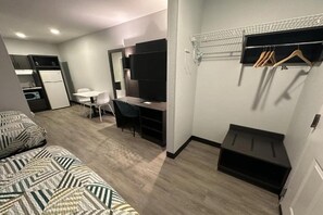 Ett kompakt hotellrum med en säng, skrivbord, stol och ett litet pentry.