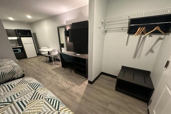 A compact hotel room with a bed, desk, chair, and a small kitchenette.