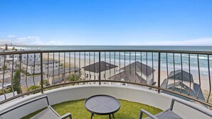 Ein Balkon mit Blick auf Strand und Meer, ein kleiner runder Tisch und eine Rasenfläche.