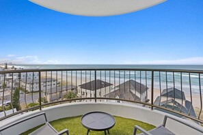 Ein Balkon mit Blick auf Strand und Meer, ein kleiner runder Tisch und eine Rasenfläche.