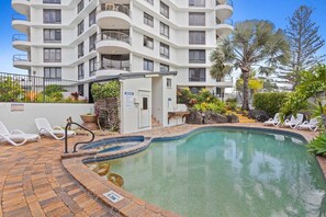 A multi-story residential building with a swimming pool, outdoor seating, and a notice board. - Seascape Serenity in Palm Beach (Gold Coast)