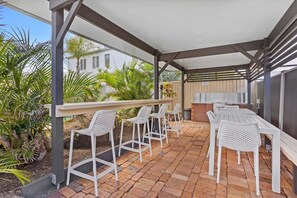 An outdoor patio with white metal chairs and a table, a barbecue area, and a view of a house. - Seascape Serenity in Palm Beach (Gold Coast)