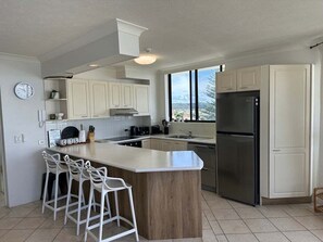Eine moderne Küche mit einer zentralen Kochinsel, Barhocker, einem Edelstahlkühlschrank und einem Fenster mit Blick.