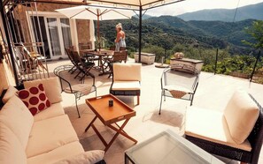 Eine Terrasse im Freien mit Sitzgelegenheiten, einem Tisch und Blick auf eine gebirgige Landschaft.