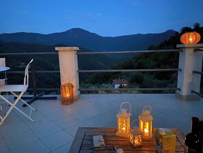 Eine Terrasse mit Tisch, Stühlen und Laternen mit Blick auf eine gebirgige Landschaft.